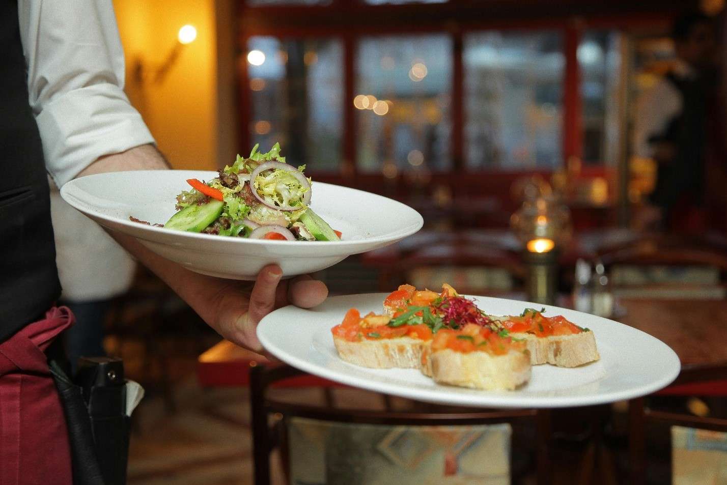 A Waiter in a Warm, Softly Lit Restaurant Presents Two Elegant Dishes