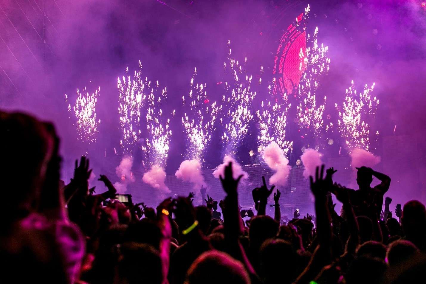 An Energetic Concert Scene with a Crowd of People Silhouetted Against a Vibrant Display of Pink Fireworks and Stage Lights