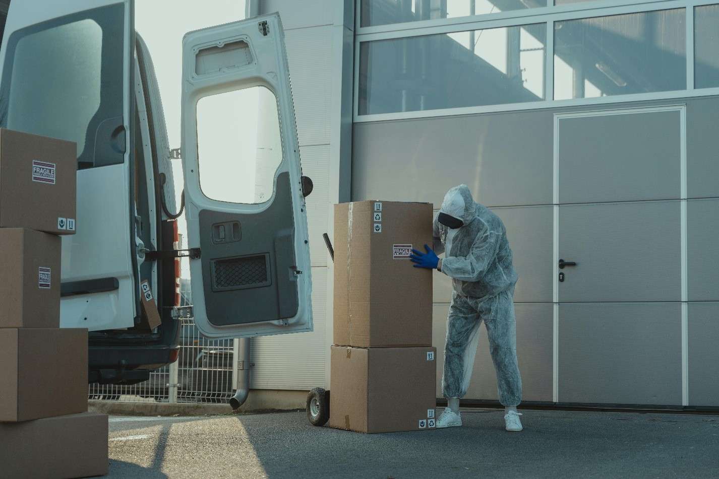 A Worker Is Carefully Handling a Stack of Labeled Cardboard Boxes Next to an Open Cargo Van